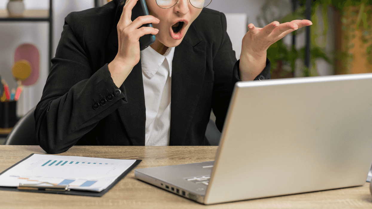 Woman screaming into her phone while looking at her laptop.