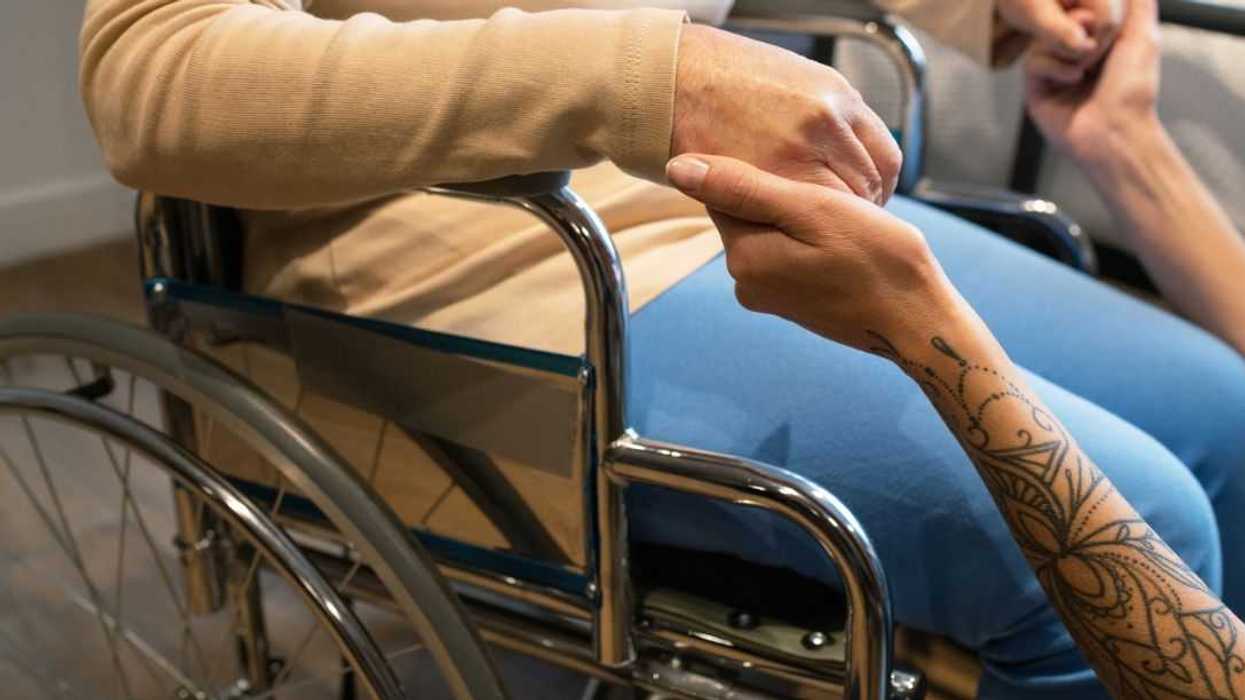 Woman seated in wheelchair and holding hands of healthcare professional after moving from bed to mode of transport.