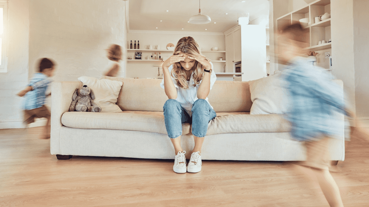 woman seatedon couch with headin hands as kids run around