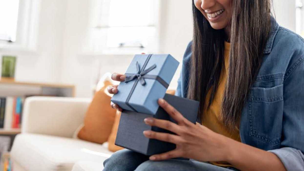 Woman smiling while opening a birthday present at home.