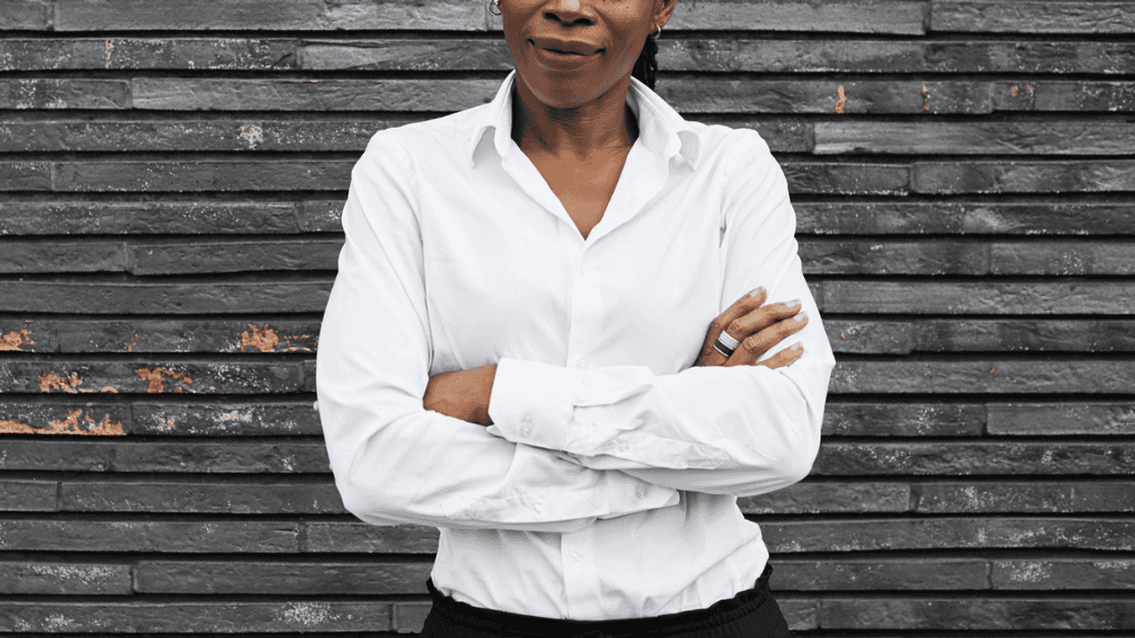 woman standing front of wooden wall wearing white shirt and black pants