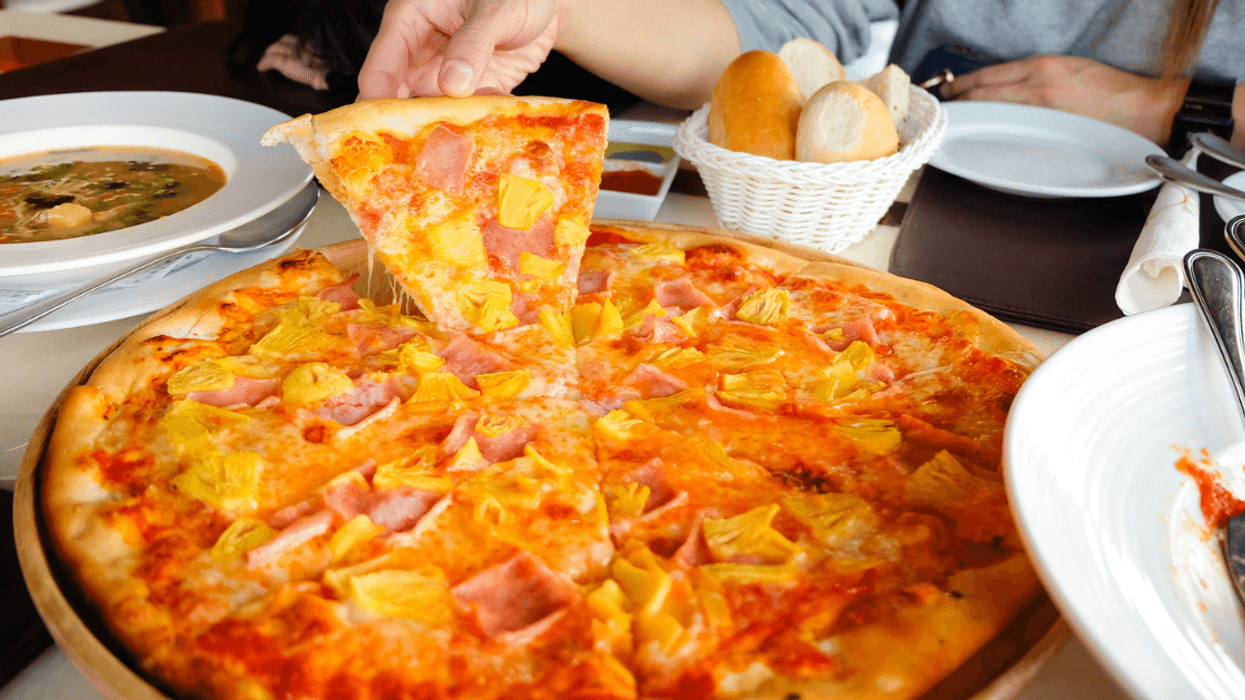 Woman taking a slice of Hawaiian Pizza.