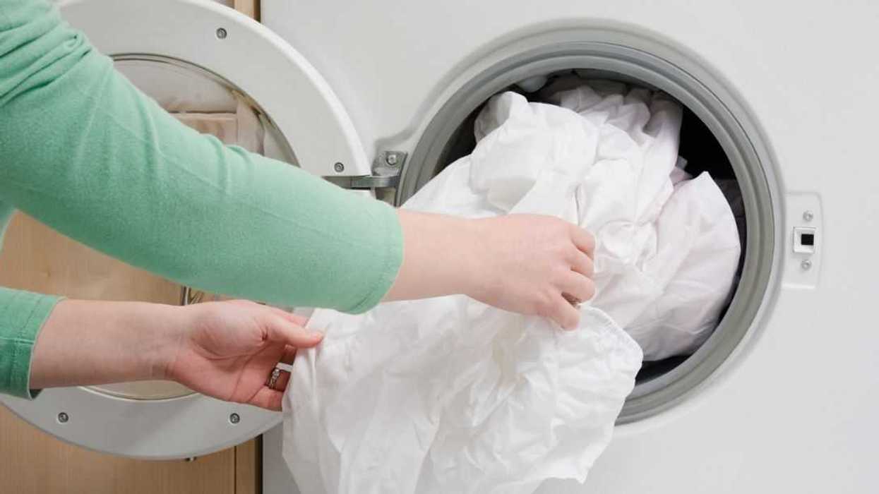 Woman taking sheet from washing machine.