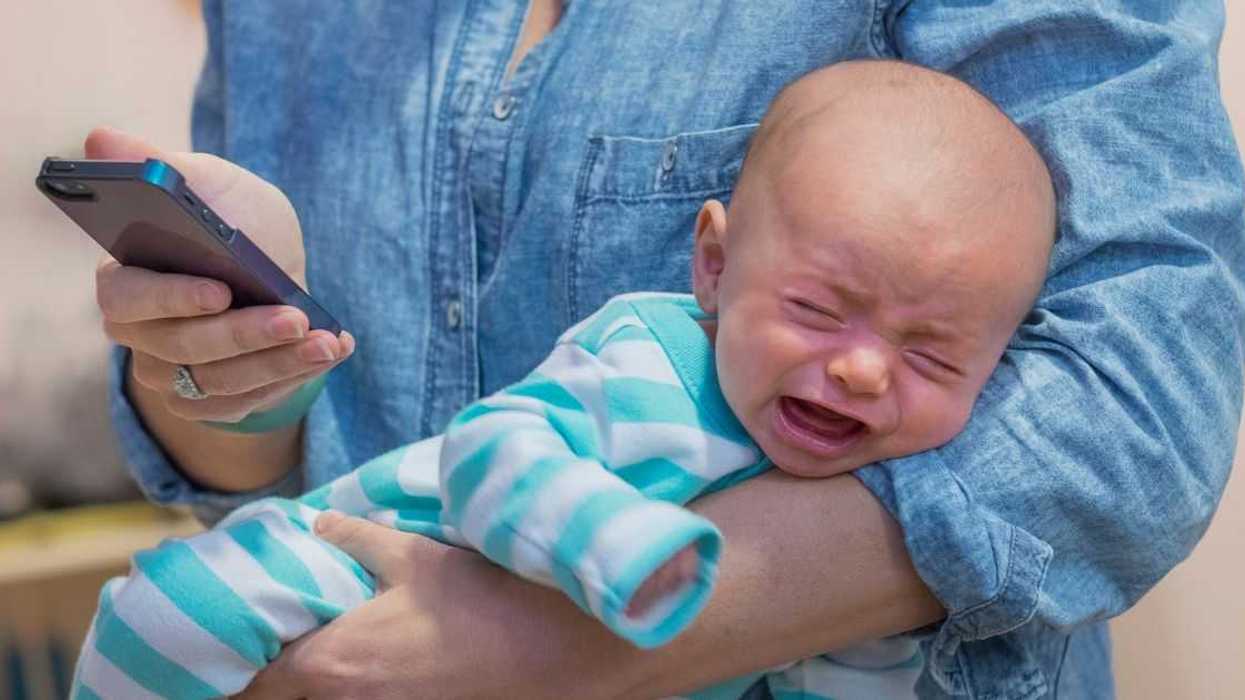 Woman texting and holding crying baby boy