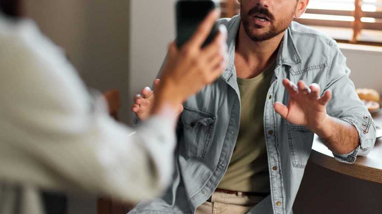 Worried man explaining himself to his girlfriend who found some suspicious text messages on his cell phone.