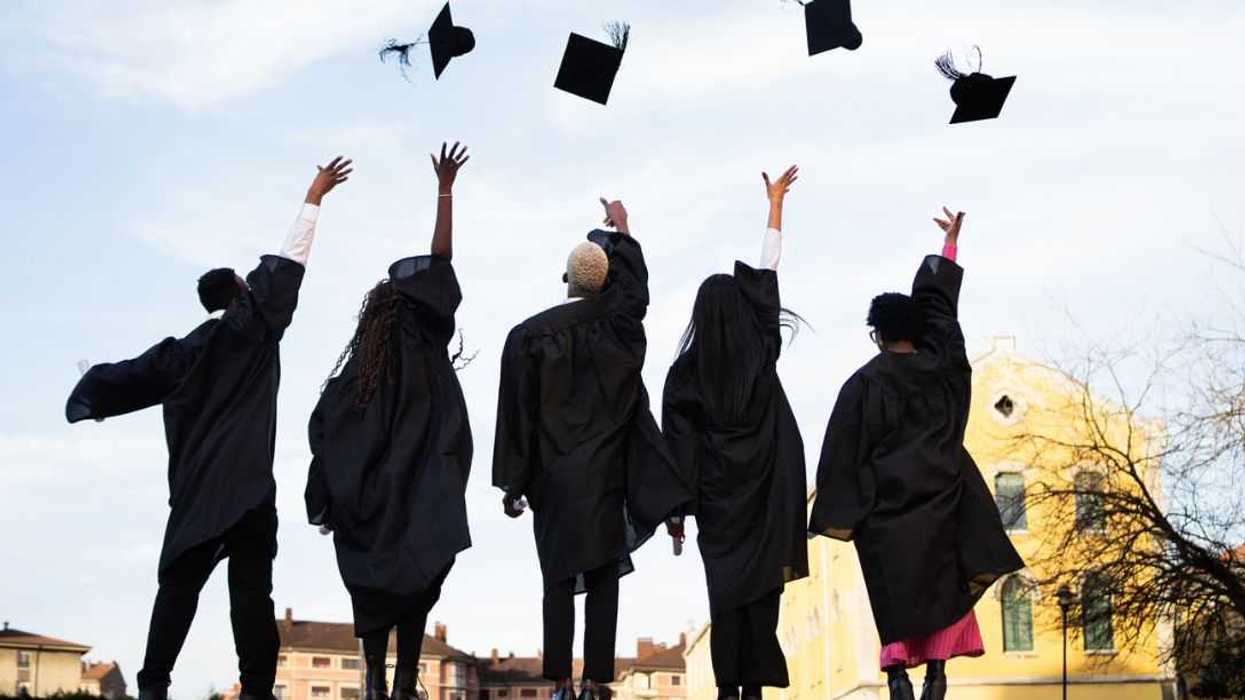 Young adults in graduation gowns joyfully tossing caps into the sky, celebrating achievement and new beginnings against a clear backdrop.