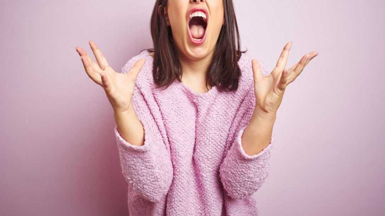 Young beautiful brunette woman wearing a pink sweater over pink isolated background crazy and mad shouting and yelling with aggressive expression and arms raised. Frustration concept.