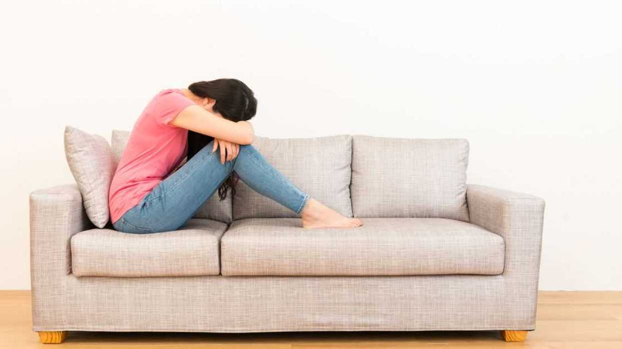Young, beautiful woman sadly sitting on the sofa with her head in her lap.