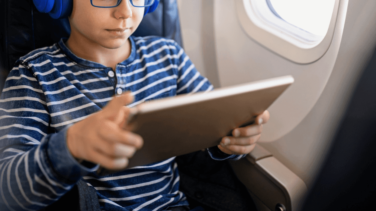 young boy seated on airplane looking at tablet
