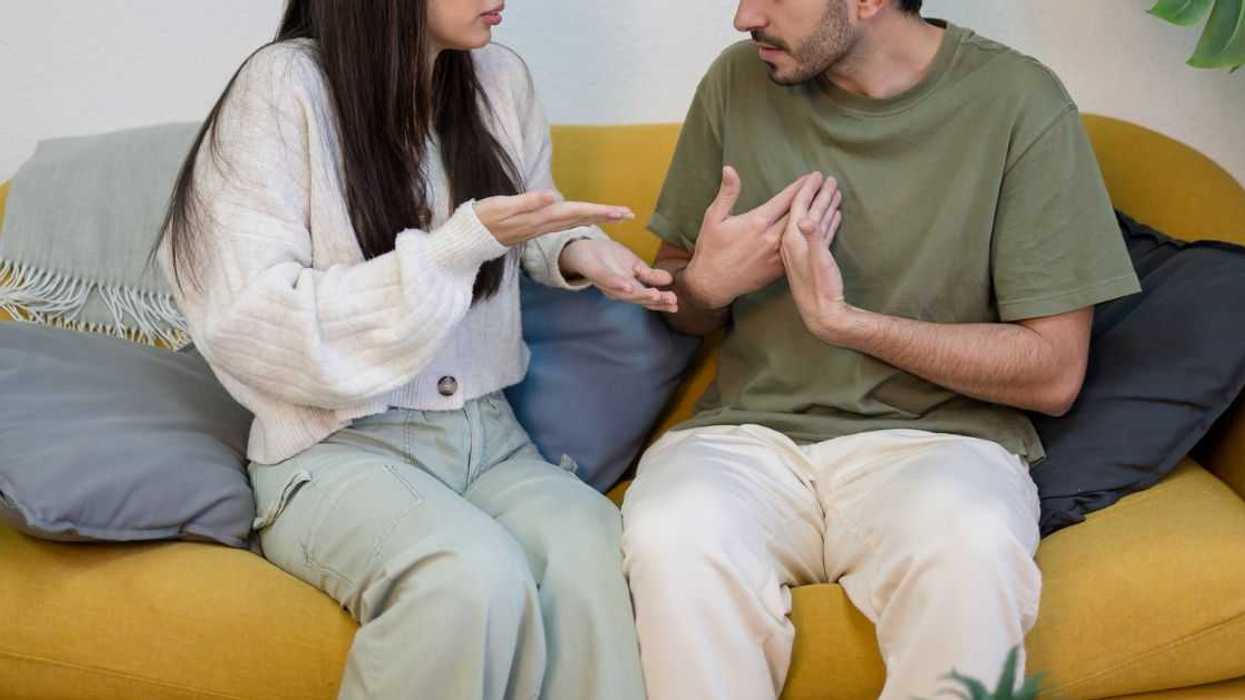 Young boyfriend and girlfriend sitting on sofa near potted plant and quarreling while having problems in relationship.