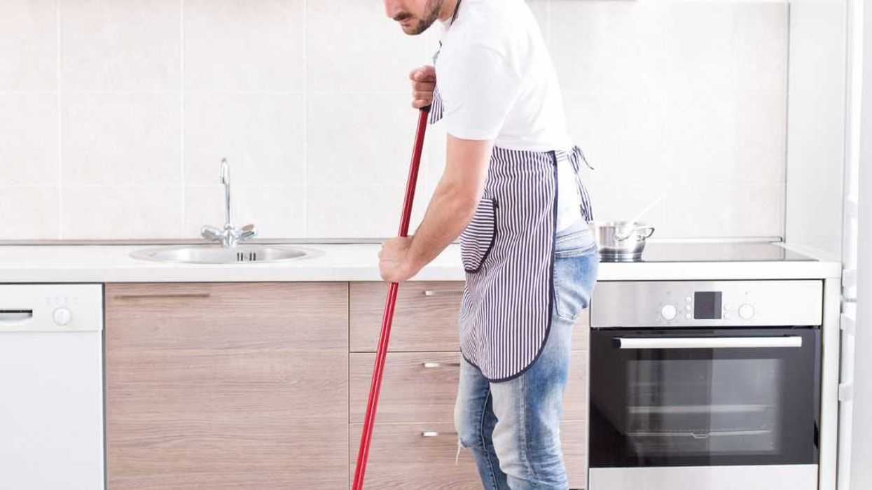 Young handsome man mopping tiled floor in kitchen. Husband housework concept.