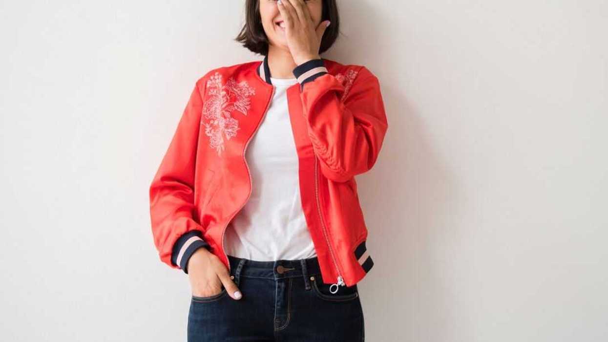 Young laughing woman wearing a red jacket leans on a wall.