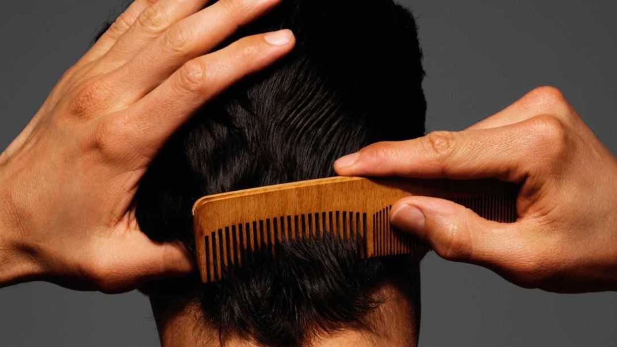 Young man combing back of head, rear view.