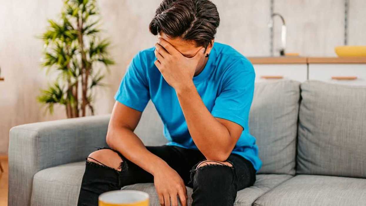 Young Man Sitting At Home Looking Sad And Distraught