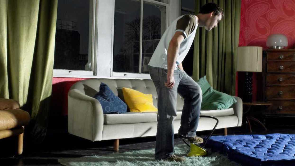 Young man using foot pump on air mattress in living room.