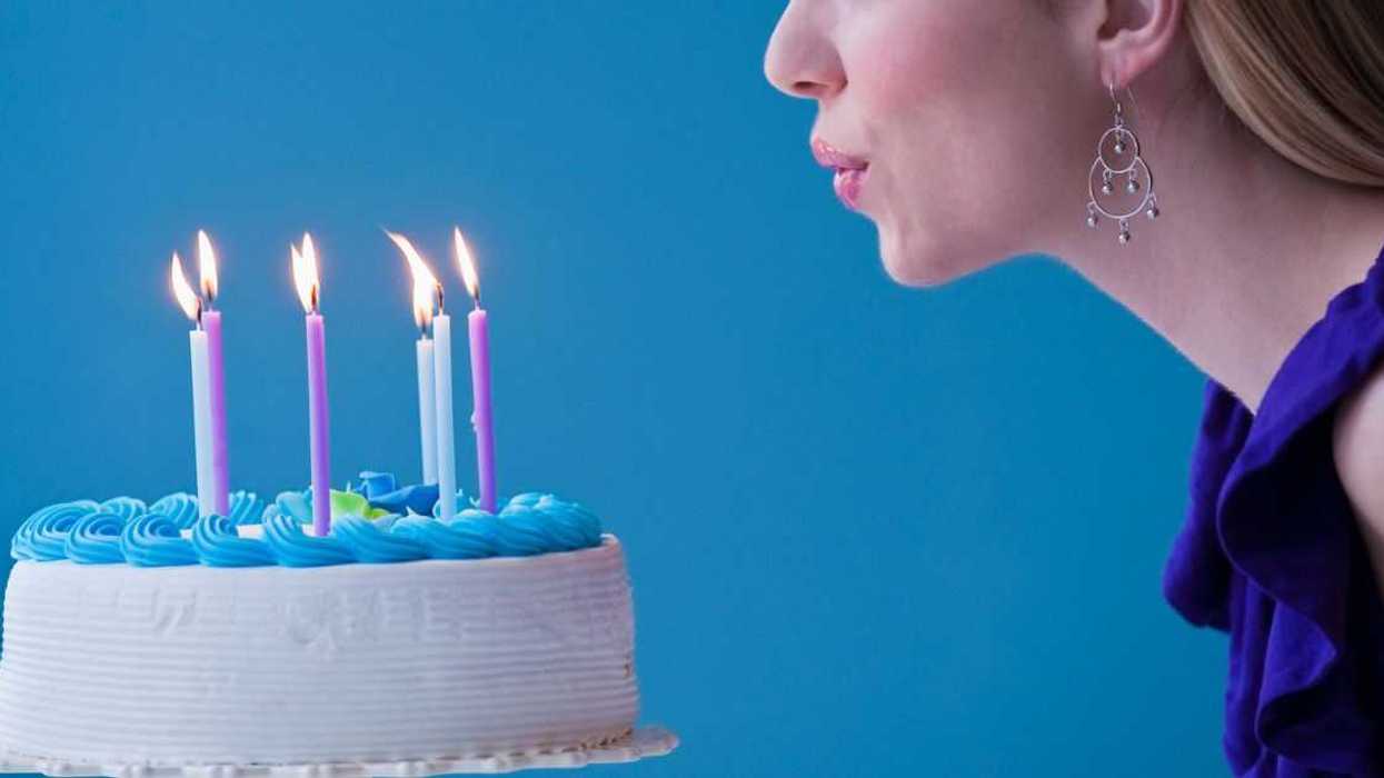 Young woman blowing out candles on a birthday cake, studio shot, light blue background.