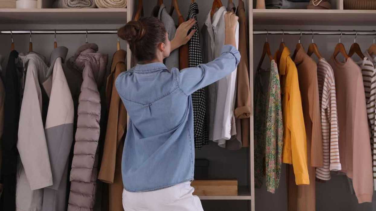 Young woman choosing clothes in wardrobe closet, back view.