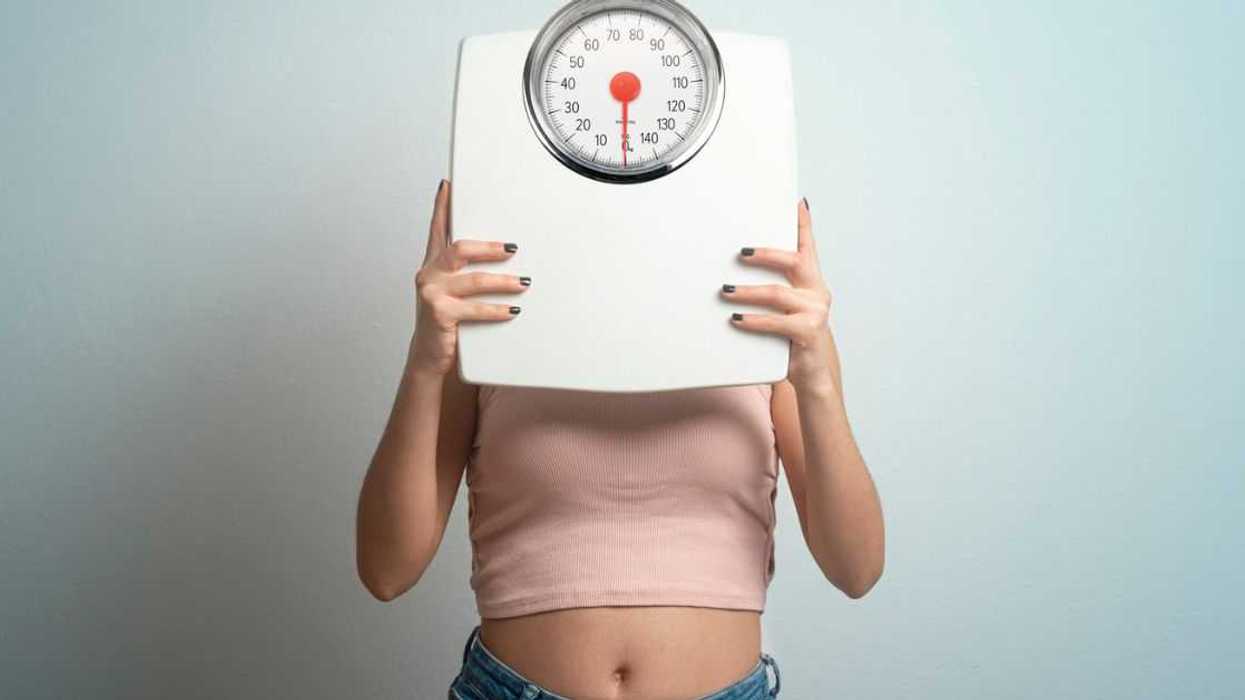 Young woman hides her face behind a bathroom scale. Studio shot.