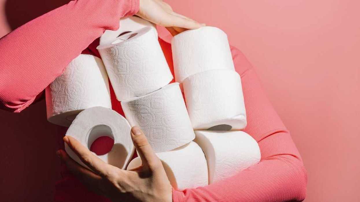 Young woman holding many toilet tissue paper rolls in bright pink sweater on pink background.