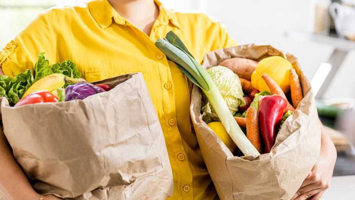 Young woman is carrying two paper bags of vegetables at home.