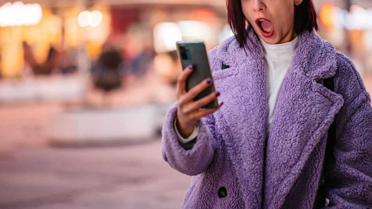 Young woman receiving a surprising text message while on the city street.