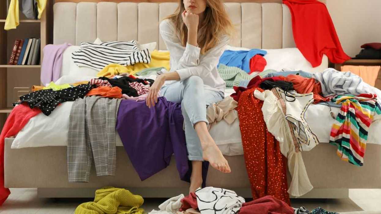 Young woman surrounded by different clothes in a messy room. Fast fashion concept