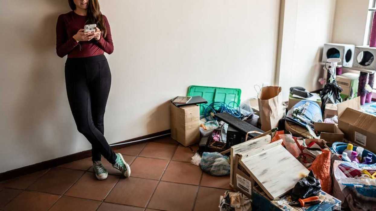 Young woman using mobile phone during house moving at the new apartment.