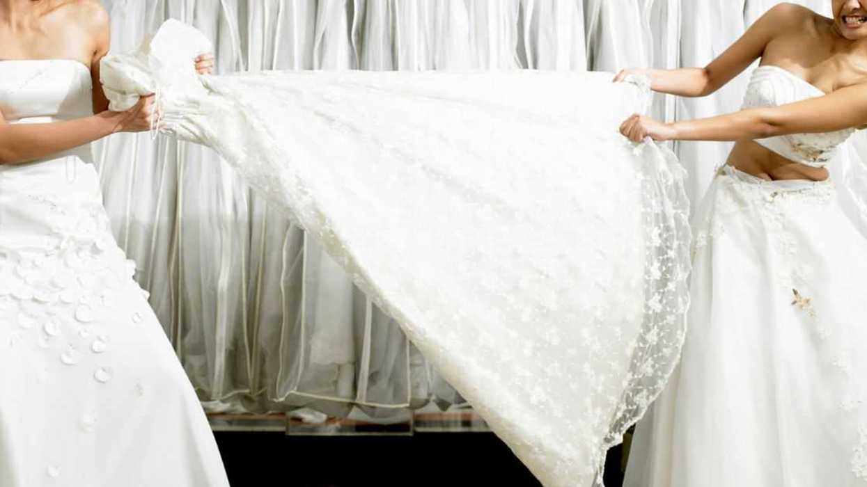 Young women in fitting room tugging at gown.