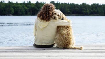 woman cuddles her dog on a dock by the water