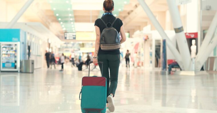 A woman walk threw an airport with a suitcase