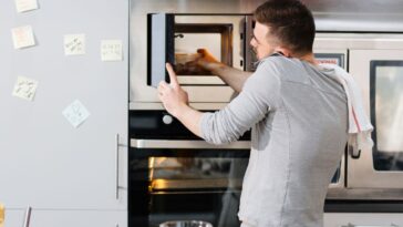 A guy puts food in a microwave, while on the phone