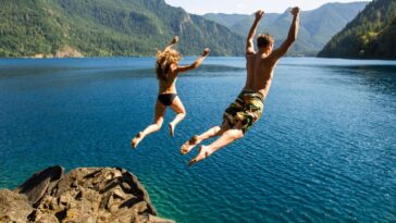 A couple with their backs facing to the camera jumps off a cliff into the ocean