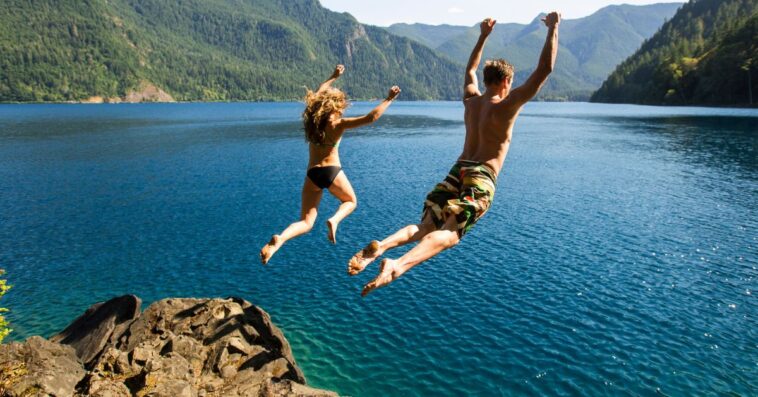 A couple with their backs facing to the camera jumps off a cliff into the ocean