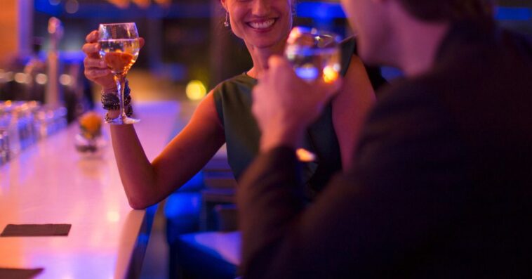 A man and woman drink and flirt in a dimly lit bar