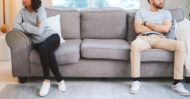 A mixed race couple sit across from one another on a couch, clearly not speaking