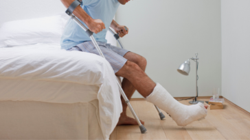 man with broken leg and crutches sitting on bed