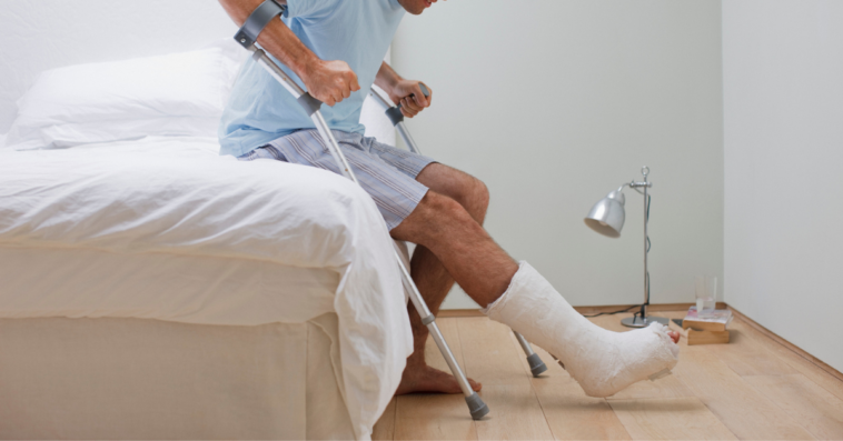 man with broken leg and crutches sitting on bed