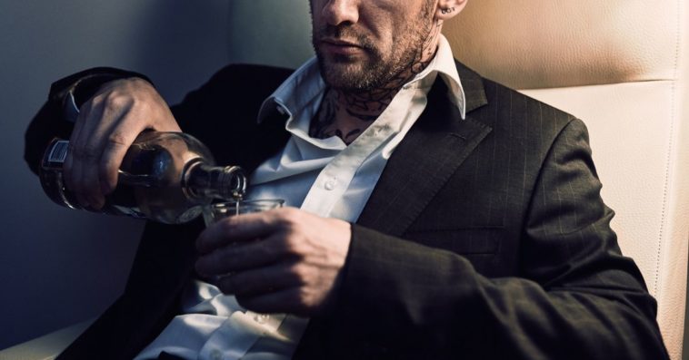A man sits, a bit sullen, and pours vodka