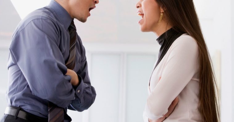 A man and woman squabble face to face at work
