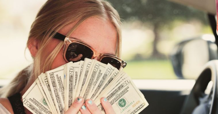 A woman wearing sunglasses holds out a ton of cash