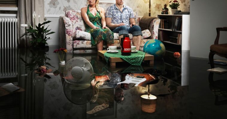 A couple sits on a couch in the middle of a messy house