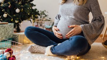 A pregnant woman sits in front of a Christmas tree
