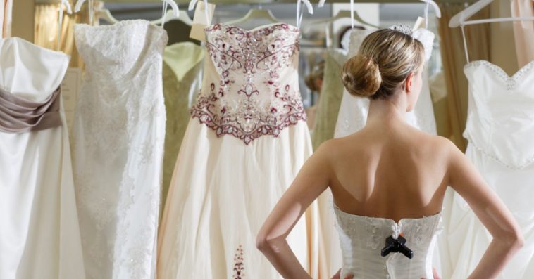 A bride stand before several dresses to choose from
