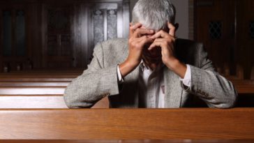 Man holding heads in church pew.