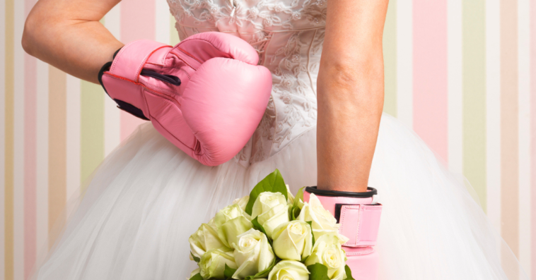 Woman in wedding dress, wearing boxing gloves and holding flowers