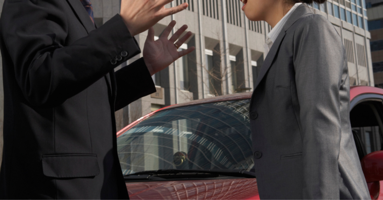 Two people arguing in front of a car.