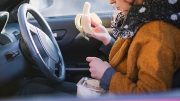A woman eats a banana and sandwich in a car in winter