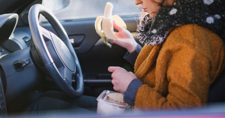 A woman eats a banana and sandwich in a car in winter