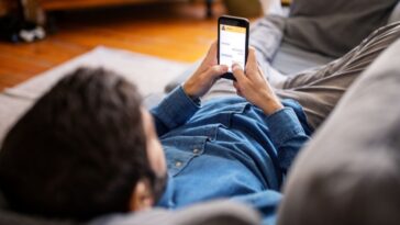A man lays on the couch while phone scrolling
