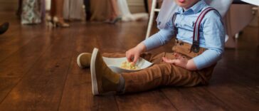 A little boy sits on the floor of a wedding eating food